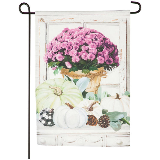 In front of a white washed window panel is a table with a basket of purple mums and various pumpkins.