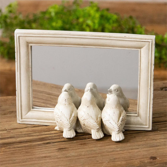 Small tabletop mirror is freestanding in a white distressed finish with a trio of three little birds peeking at their reflections.  The mirror is make of polyresin and measures 8.25 inches wide by 2.25 inches deep by 6 inches high.