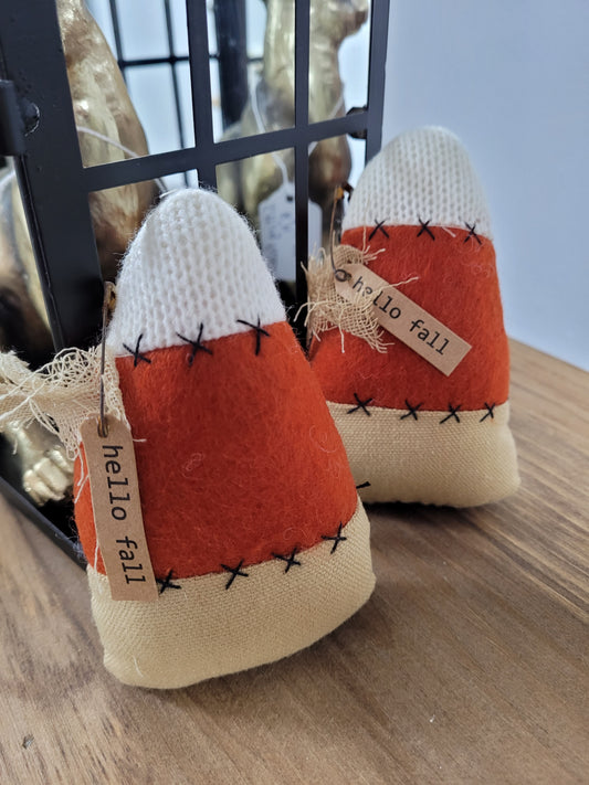 This Plush Candy Corn Fall Décor is approximately 5 inches high and  3 inches wide at the bottom with an attached tag that says Hello Fall.  The colors are traditional candy corn with a beige  bottom, orange middle and a white top.