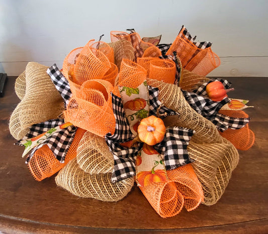 This pretty handmade fall centerpiece or candle ring can be used on a table, mantel, desk or counter. It is made of tan and orange deco mesh, black and white ribbon, pumpkin ribbon, and faux small pumpkins. The centerpiece measures 16x16x6 inches.  Add a fall colored  LED pillar candle in the center for a charming festive effect.